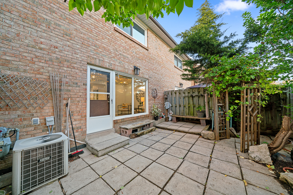 Private backyard patio paved with concrete slabs, enclosed by a wooden privacy fence with a vine-covered trellis arch