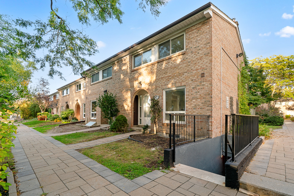 Corner unit seen from the sidewalk with arched entry, exterior stairwell and mature trees