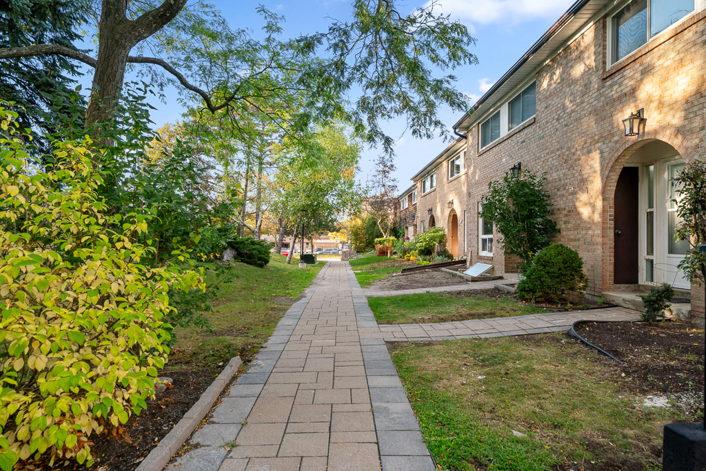 Paved walkway running past the row of tan brick townhomes under a clear sky